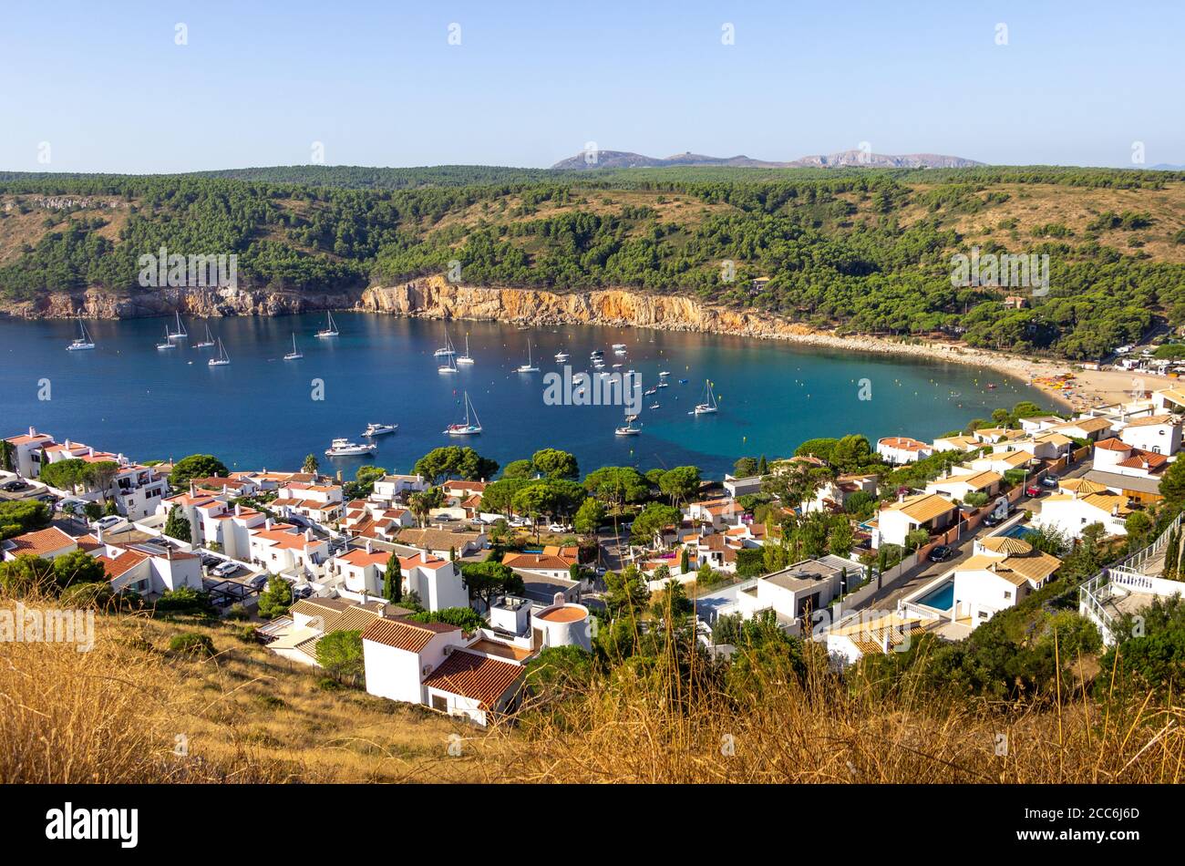 Looking down over Cala Montgó with blue water, boats, holiday homes and red cliffs in summer, L'Escala, Costa Brava, Girona, Catalonia, Spain Stock Photo