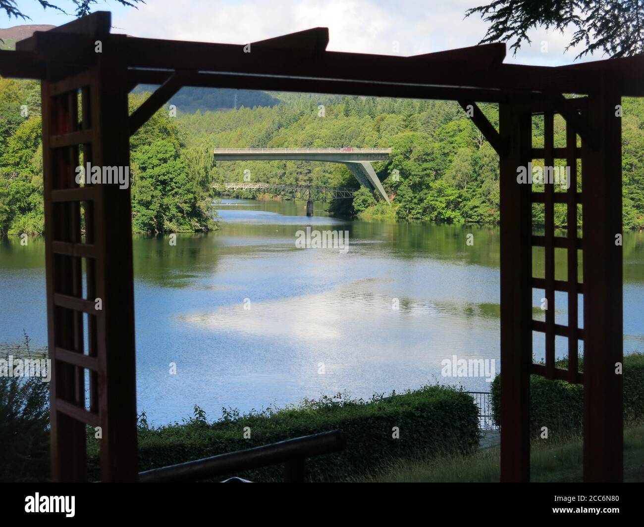 Framed by a latticed pergola, a view overlooking Loch Faskally in Highland Perthshire with the road and pedestrian bridges to Pitlochry. Stock Photo