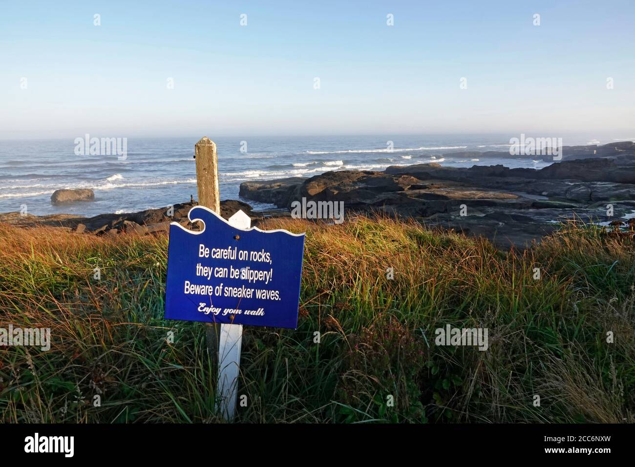 A sign warning visitors and hikers about sneaker waves on a coastal pathway along the Oregon Pacific Coast near the town of Yachats, Oregon. Stock Photo