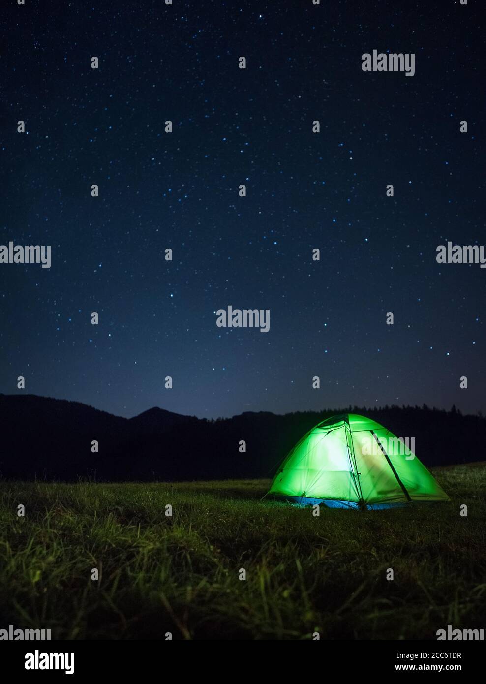 Camping tent with light inside is on the mountain valley under night starry sky Stock Photo