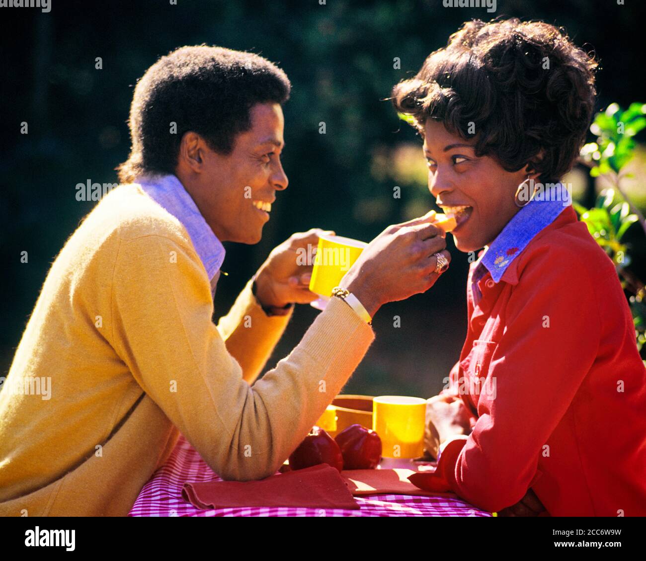 1980s SMILING AFRICAN-AMERICAN COUPLE HUSBAND AND WIFE EATING SHARING BREAKFAST MEAL FOOD TOGETHER OUTDOORS IN BRIGHT SUNLIGHT - cd00287 CAM001 HARS 1 COMMUNICATION YOUNG ADULT BALANCE STRONG PLEASED JOY LIFESTYLE FEMALES MARRIED SPOUSE HUSBANDS HEALTHINESS HOME LIFE COPY SPACE HALF-LENGTH LADIES PERSONS CARING MALES PARTNER TEMPTATION HAPPINESS BRIGHT WELLNESS CHEERFUL AFRICAN-AMERICANS AFRICAN-AMERICAN AND CAM001 BLACK ETHNICITY IN SMILES CONNECTION CONCEPTUAL JOYFUL STYLISH PERSONAL ATTACHMENT AFFECTION EMOTION WIVES YOUNG ADULT MAN YOUNG ADULT WOMAN OLD FASHIONED AFRICAN AMERICANS Stock Photo