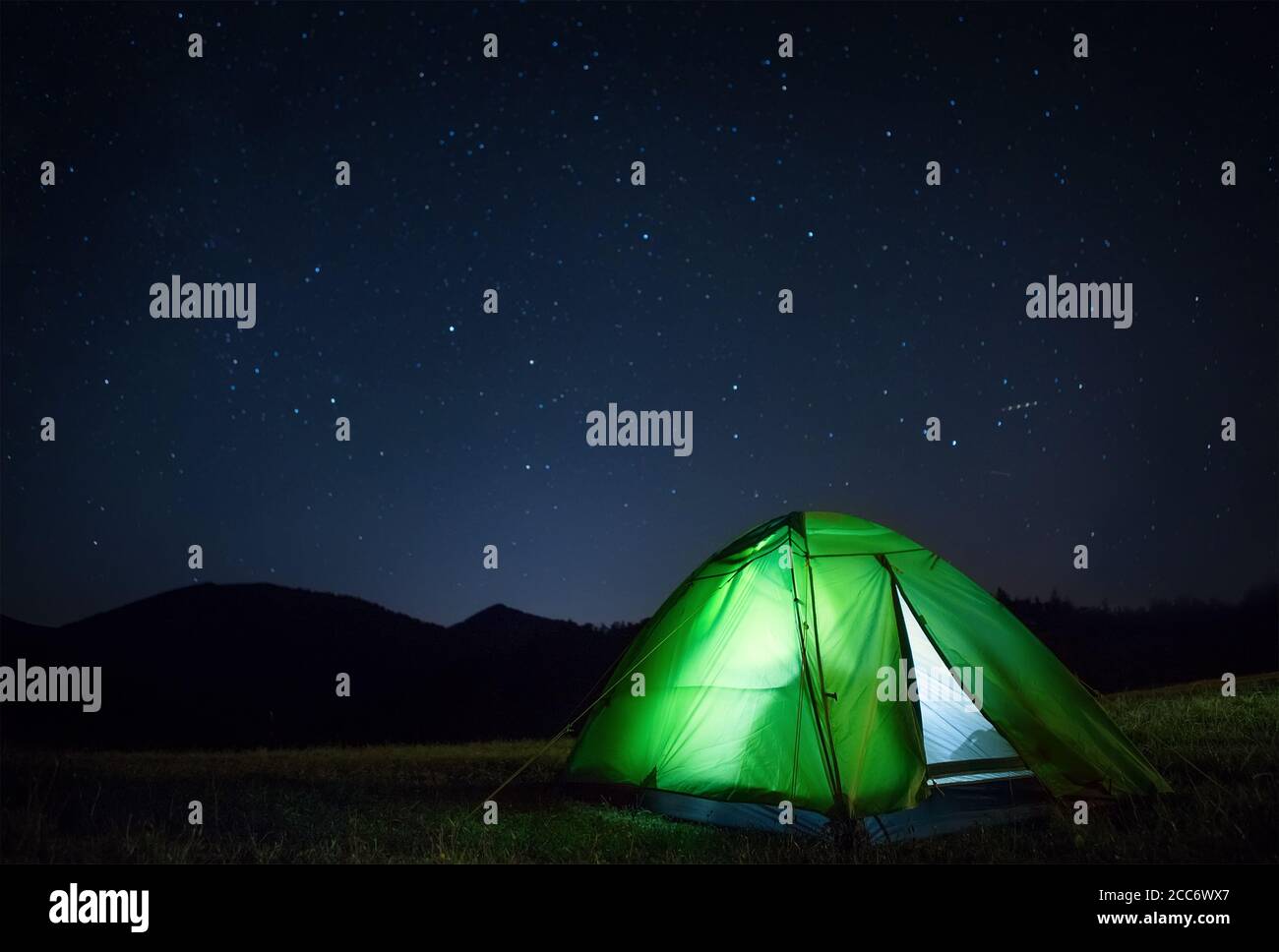 Camping tent with light inside is on the mountain valley under night starry sky Stock Photo