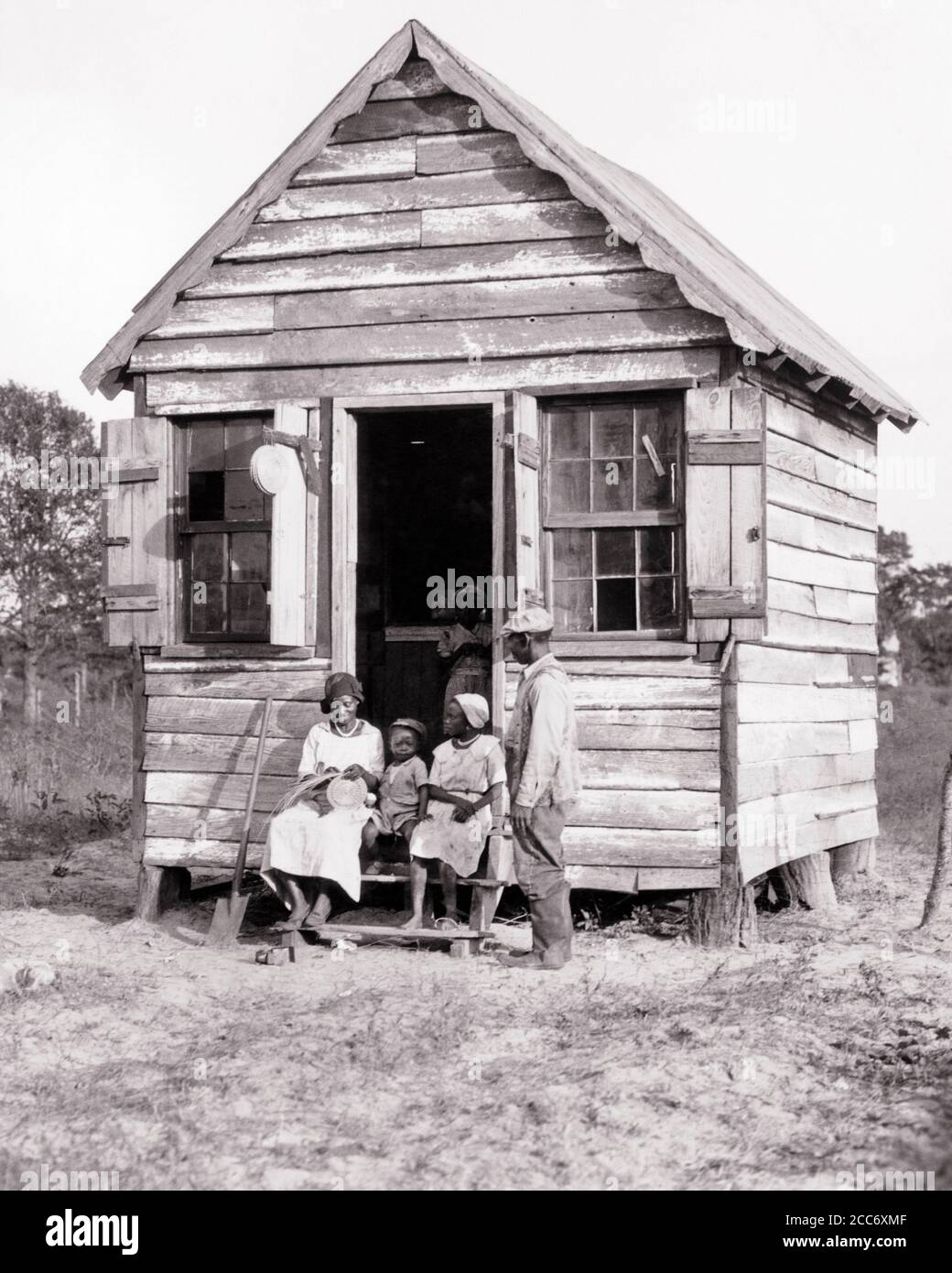 1930s 1940s AFRICAN-AMERICAN GULLAH FAMILY SITTING ON STEPS SMALL SHACK GRANDMOTHER WEAVING SWEETGRASS BASKET SOUTH CAROLINA USA - n1205 HAR001 HARS COMMUNITY STEPS GRANDMOTHER OLD TIME BUSY NOSTALGIA OLD FASHION 1 JUVENILE YOUNG ADULT SONS GRANDPARENTS FAMILIES LIFESTYLE CELEBRATION FEMALES HOUSES MARRIED GRANDPARENT RURAL SPOUSE HUSBANDS UNITED STATES COPY SPACE FULL-LENGTH LADIES PERSONS TRADITIONAL RESIDENTIAL UNITED STATES OF AMERICA MALES BUILDINGS CRAFT SPIRITUALITY B&W PARTNER SADNESS TODDLERS NORTH AMERICA NORTH AMERICAN SOUVENIR STRENGTH CUSTOMER SERVICE AFRICAN-AMERICANS Stock Photo