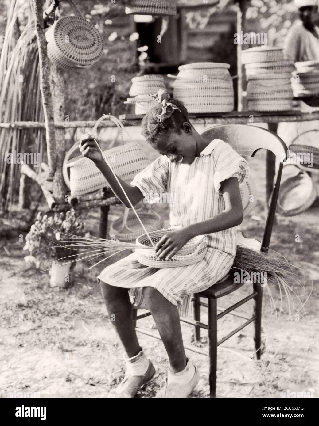 1930s 1940s ANONYMOUS SMILING YOUNG AFRICAN-AMERICAN GULLAH GIRL WEAVING MAKING BASKET FROM SWEETGRASS SOUTH CAROLINA USA - n1204 HAR001 HARS NOSTALGIA OLD FASHION 1 JUVENILE CAREER LIFESTYLE CELEBRATION FEMALES JOBS RURAL HEALTHINESS HOME LIFE UNITED STATES COPY SPACE FULL-LENGTH HIGHWAY PERSONS INSPIRATION TRADITIONAL UNITED STATES OF AMERICA TEENAGE GIRL PROFESSION CRAFT SPIRITUALITY CONFIDENCE B&W SADNESS NORTH AMERICA NORTH AMERICAN GEORGIA SKILL OCCUPATION HAPPINESS SKILLS LANGUAGE WELLNESS STRENGTH CUSTOMER SERVICE AFRICAN-AMERICANS AFRICAN-AMERICAN CAREERS KNOWLEDGE TOURIST Stock Photo