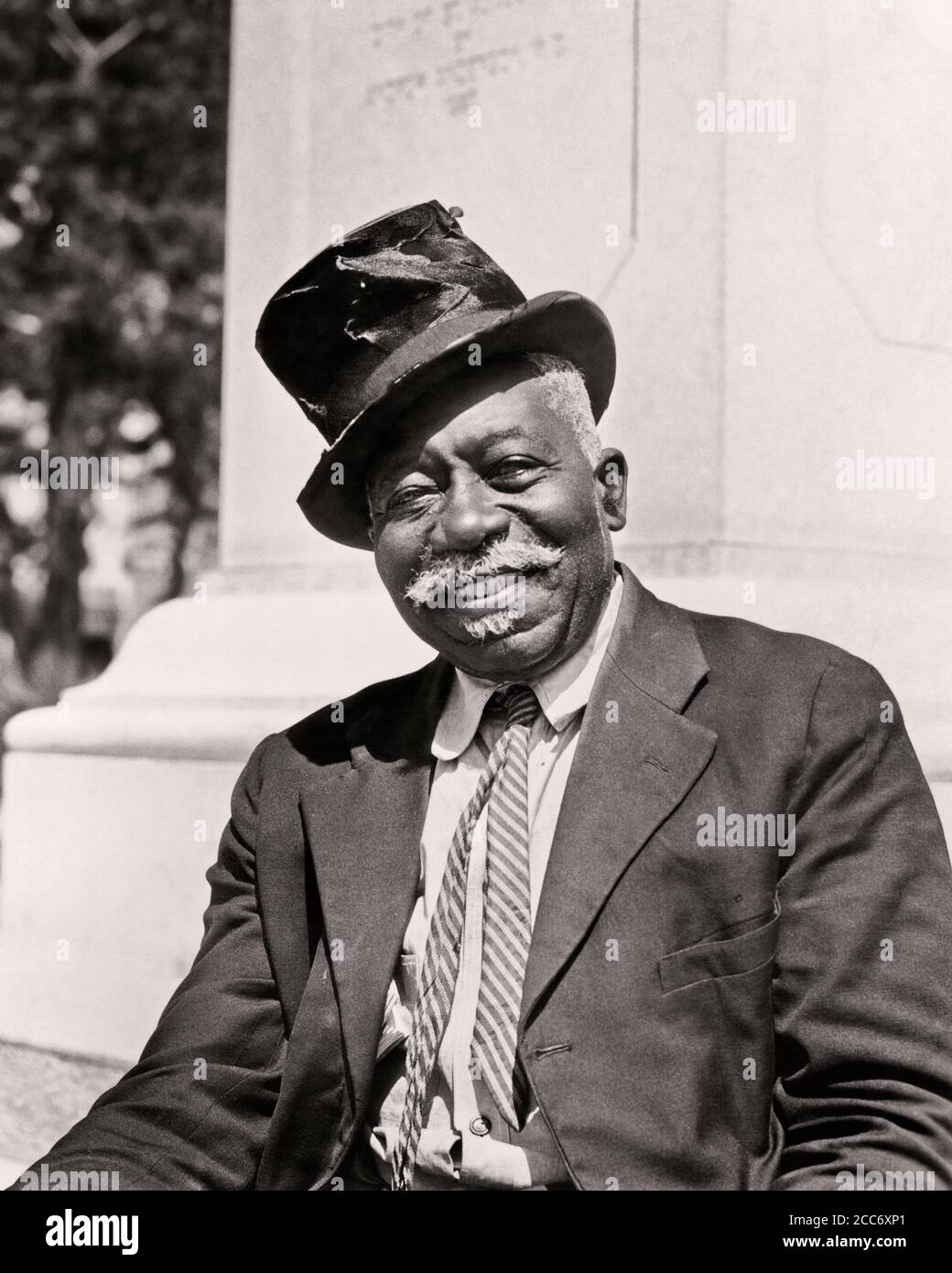 1930s SMILING AFRICAN-AMERICAN SENIOR MAN WEARING TOP HAT COAT TIE TOURIST COACHMAN LOOKING AT CAMERA ST. AUGUSTINE FLORIDA USA - n18 HAR001 HARS COPY SPACE HALF-LENGTH UNITED STATES OF AMERICA CHARACTER CONFIDENCE SENIOR MAN TRANSPORTATION SENIOR ADULT B&W NORTH AMERICA EYE CONTACT NORTH AMERICAN MUSTACHE SKILL SUIT AND TIE OCCUPATION HAPPINESS SKILLS CHEERFUL CUSTOMER SERVICE MUSTACHES AFRICAN-AMERICANS AFRICAN-AMERICAN TOURIST BLACK ETHNICITY PRIDE AUTHORITY FACIAL HAIR OCCUPATIONS SMILES CONCEPTUAL GUIDE JOYFUL STYLISH JOVIAL ST. AUGUSTINE TEAMSTER BATTERED FL BLACK AND WHITE HAR001 Stock Photo