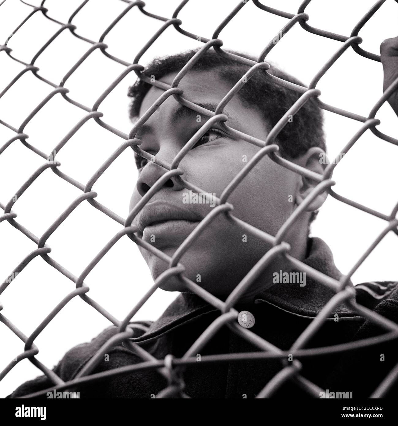 1960s WORRIED CONCERNED SINGLE AFRICAN-AMERICAN TEENAGE BOY LOOKING THRU A CHAIN-LINK FENCE THINKING ABOUT AN UNCERTAIN FUTURE - n1934 HAR001 HARS ANGER FEAR WORRY LIFESTYLE MOODY POOR HOME LIFE COPY SPACE HALF-LENGTH PERSONS MALES RISK TEENAGE BOY ABOUT EXPRESSIONS TROUBLED B&W CONCERNED SADNESS FREEDOM GOALS DREAMS HEAD AND SHOULDERS AFRICAN-AMERICANS AFRICAN-AMERICAN LOW ANGLE BLACK ETHNICITY A AN MOOD CONCEPTUAL GLUM DEPRIVED ESCAPE TEENAGED DENIED DISADVANTAGED LOOKING IN BARRIER CHAIN-LINK CONFINED DISAFFECTED DISAPPOINTED DISCONNECTED GROWTH IMPOVERISHED JUVENILES MISERABLE TRAPPED Stock Photo