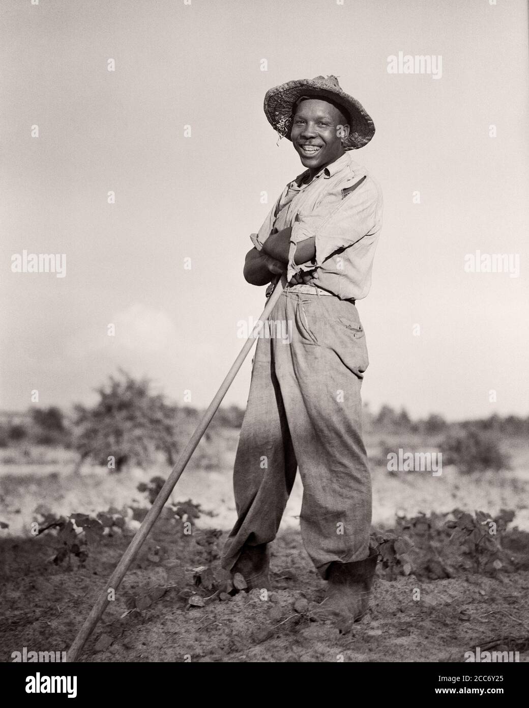 1930s SMILING AFRICAN-AMERICAN MAN TOBACCO FARMER WEARING STRAW HAT STANDING LEANING ON HOE LOOKING AT CAMERA NORTH CAROLINA USA - n68 HAR001 HARS 1 FACIAL LAUGH PLEASED JOY LIFESTYLE SATISFACTION JOBS POOR RURAL UNITED STATES COPY SPACE FULL-LENGTH PERSONS UNITED STATES OF AMERICA FARMING MALES CONFIDENCE EXPRESSIONS AGRICULTURE B&W NORTH AMERICA EYE CONTACT NORTH AMERICAN SKILL OCCUPATION HAPPINESS SKILLS CHEERFUL STRENGTH TOBACCO AFRICAN-AMERICANS AFRICAN-AMERICAN FARMERS LOW ANGLE BLACK ETHNICITY LABOR PRIDE ON EMPLOYMENT OCCUPATIONS CONCEPTUAL HANDLE JOYFUL HOE SHARECROPPER EMPLOYEE Stock Photo