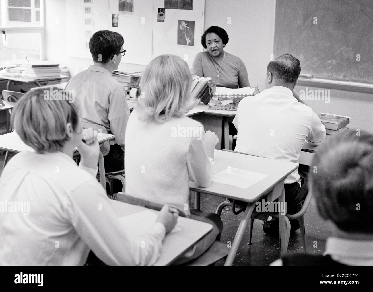 1960s BACKS OF ANONYMOUS ADULT STUDENTS IN CLASSROOM BEING TAUGHT BY A MATURE AFRICAN-AMERICAN WOMAN TEACHER SPEAKING LECTURING - s15984 HAR001 HARS MALES CONFIDENCE B&W DESKS GOALS SCHOOLS AFRICAN-AMERICANS AFRICAN-AMERICAN INSTRUCTOR KNOWLEDGE LEADERSHIP BLACK ETHNICITY REAR VIEW HIGH SCHOOL OCCUPATIONS HIGH SCHOOLS EDUCATOR ANONYMOUS BACK VIEW COOPERATION EDUCATING EDUCATORS INSTRUCTORS MID-ADULT MID-ADULT WOMAN SCHOOL TEACHES TOGETHERNESS BLACK AND WHITE CAUCASIAN ETHNICITY HAR001 OLD FASHIONED AFRICAN AMERICANS Stock Photo