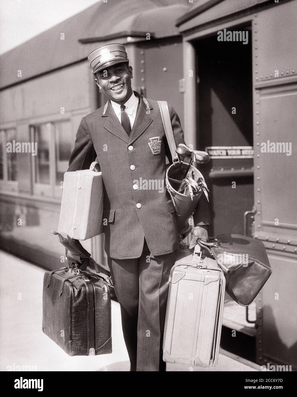 1930s SMILING AFRICAN-AMERICAN MAN RED CAP PORTER CARRYING LUGGAGE IN TRAIN  STATION - r6039 HAR001 HARS OLD TIME BUSY NOSTALGIA TRAINS INDUSTRY OLD  FASHION 1 FACIAL WELCOME LAUGH CAREER RAILROAD SUITCASES PLEASED