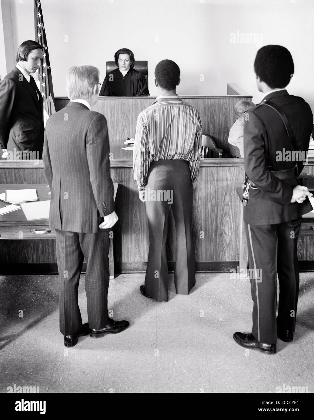 1970s COURTROOM SCENE AFRICAN-AMERICAN TEEN  BOY STANDING BEFORE FEMALE JUDGE WITH BAILIFF AND ATTORNEY - s20710 HAR001 HARS URBAN DIVERSITY JUSTICE OLD TIME FUTURE NOSTALGIA OLD FASHION 1 POLICEMAN JUVENILE LEGAL STYLE DIVERSE FEAR COMMUNICATION SERVE YOUNG ADULT TEAMWORK TROUBLE INFORMATION DIFFERENT LIFESTYLE FEMALES COPY SPACE FULL-LENGTH HALF-LENGTH LADIES TRIAL PERSONS CARING MALES RISK ORDER OFFICER TEENAGE BOY B&W SADNESS COP FREEDOM GOALS SUIT AND TIE BEFORE PROTECT PROTECTION JUDICIAL LAWYERS AFRICAN-AMERICANS AFRICAN-AMERICAN AND KNOWLEDGE LEADERSHIP POWERFUL JUDGMENT Stock Photo