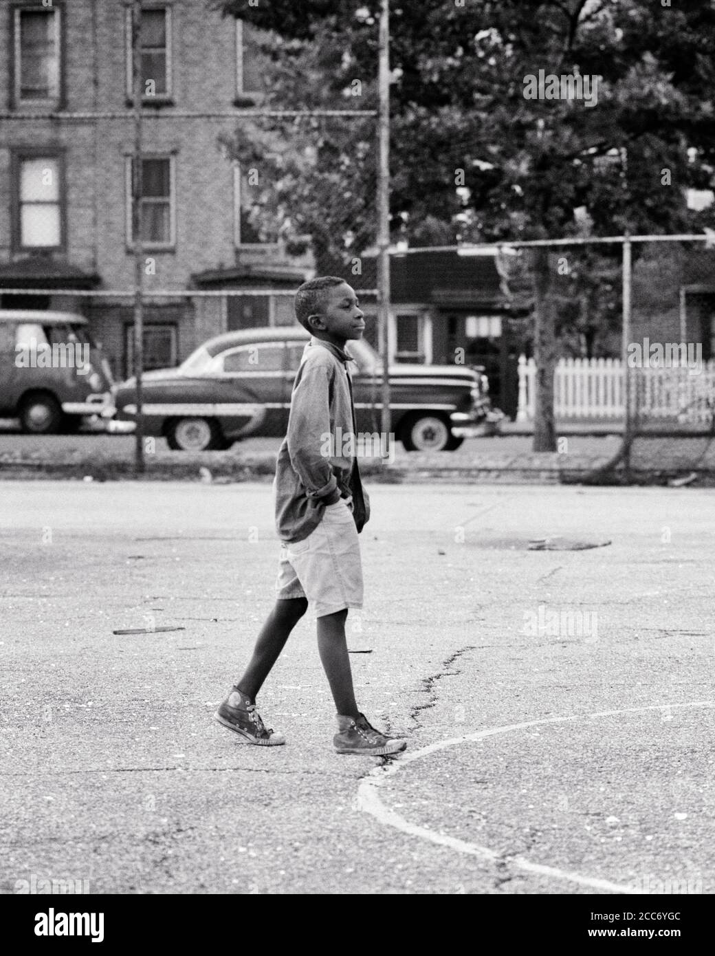 1960s 1970s ANONYMOUS ALONE AIMLESS AFRICAN-AMERICAN YOUNG MAN WALKING ACROSS ASPHALT CITY PLAYGROUND HANDS IN POCKETS NYC USA - w5858 HAR001 HARS COMMUNITY URBAN DEPRESSION OLD TIME FUTURE NOSTALGIA OLD FASHION 1 JUVENILE STYLE FEAR SECURITY PEACE SAFETY COMPETITION WORRY LIFESTYLE MOODY POOR HEALTHINESS HOME LIFE POCKETS UNITED STATES COPY SPACE FULL-LENGTH PERSONS INSPIRATION UNITED STATES OF AMERICA MALES RISK TEENAGE BOY SNEAKERS CONFIDENCE TROUBLED B&W CONCERNED SADNESS NORTH AMERICA FREEDOM NORTH AMERICAN TEMPTATION DREAMS WELLNESS STRENGTH AFRICAN-AMERICANS AFRICAN-AMERICAN RECREATION Stock Photo