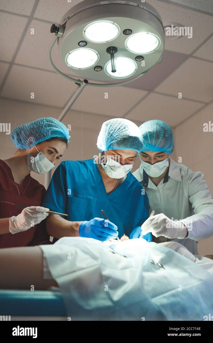 Group of surgeons at work operating in surgical theatre. Resuscitation medicine team wearing protective masks holding steel medical tools saving patie Stock Photo