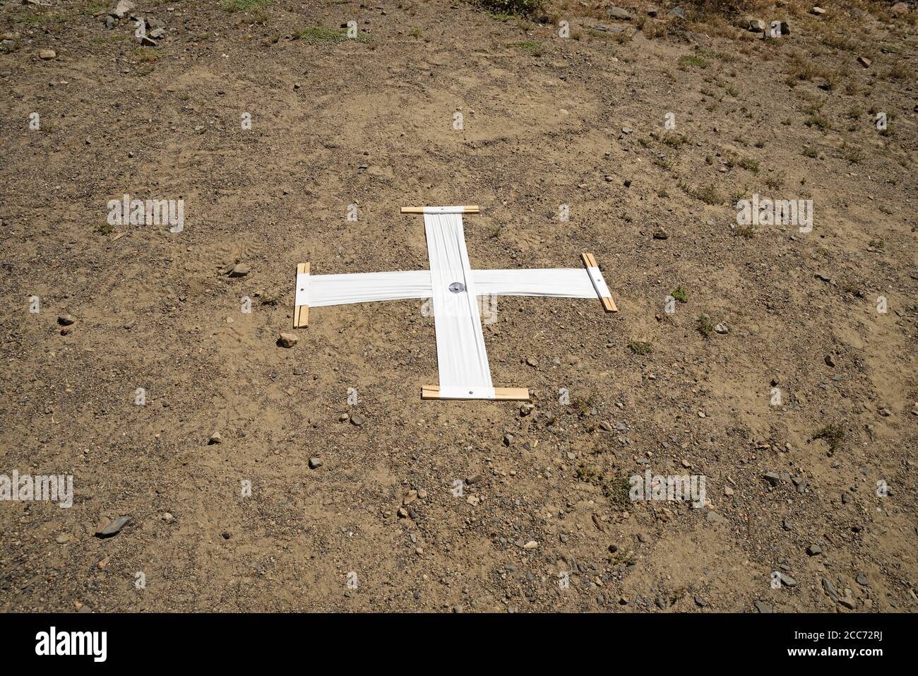 white plastic aerial survey marker cross nailed to the ground to show up in aerial photos Stock Photo