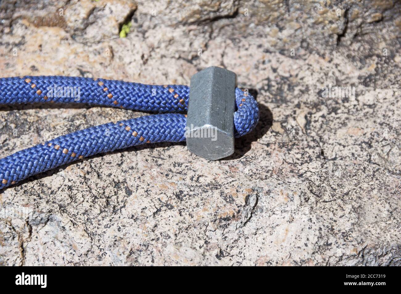 old rock climbing hex chock slung with blue cord sitting on a rock