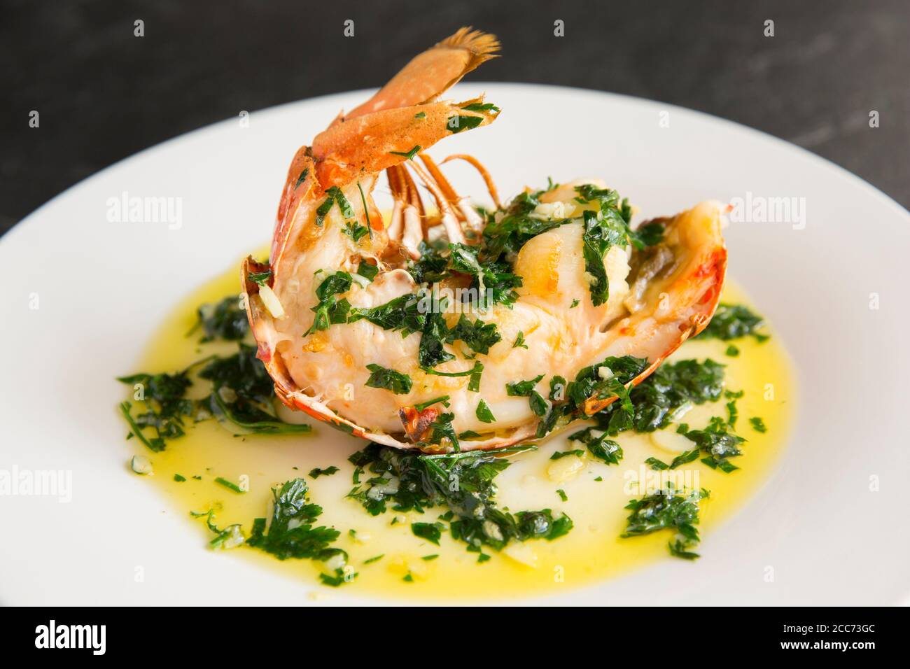 A half lobster tail, Homarus gammarus, that has been grilled and drizzled with a butter, garlic and parsley sauce. The lobster was caught in the Engli Stock Photo