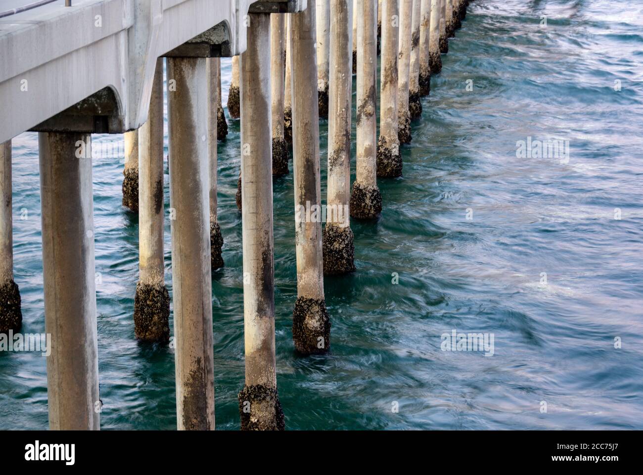 Ocean waves lapping at the concrete pilings of the Huntington Beach Pier, with exposed barnacles, at sunset in Huntington Beach, CA. Stock Photo