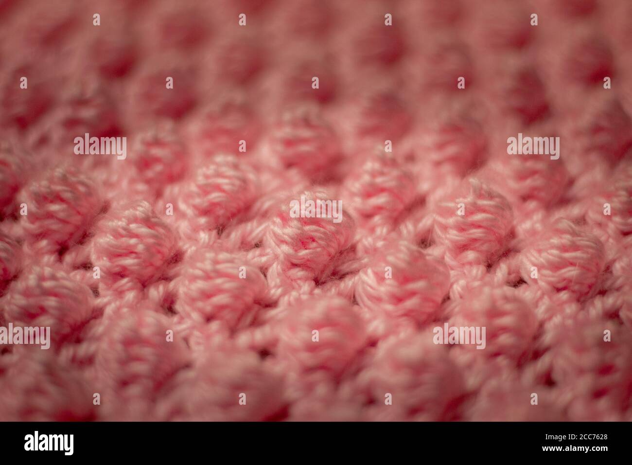 Textured pink background consisting of pink yarn crocheted baby blanket in the bobble stitch also know as the pineapple stitch Stock Photo