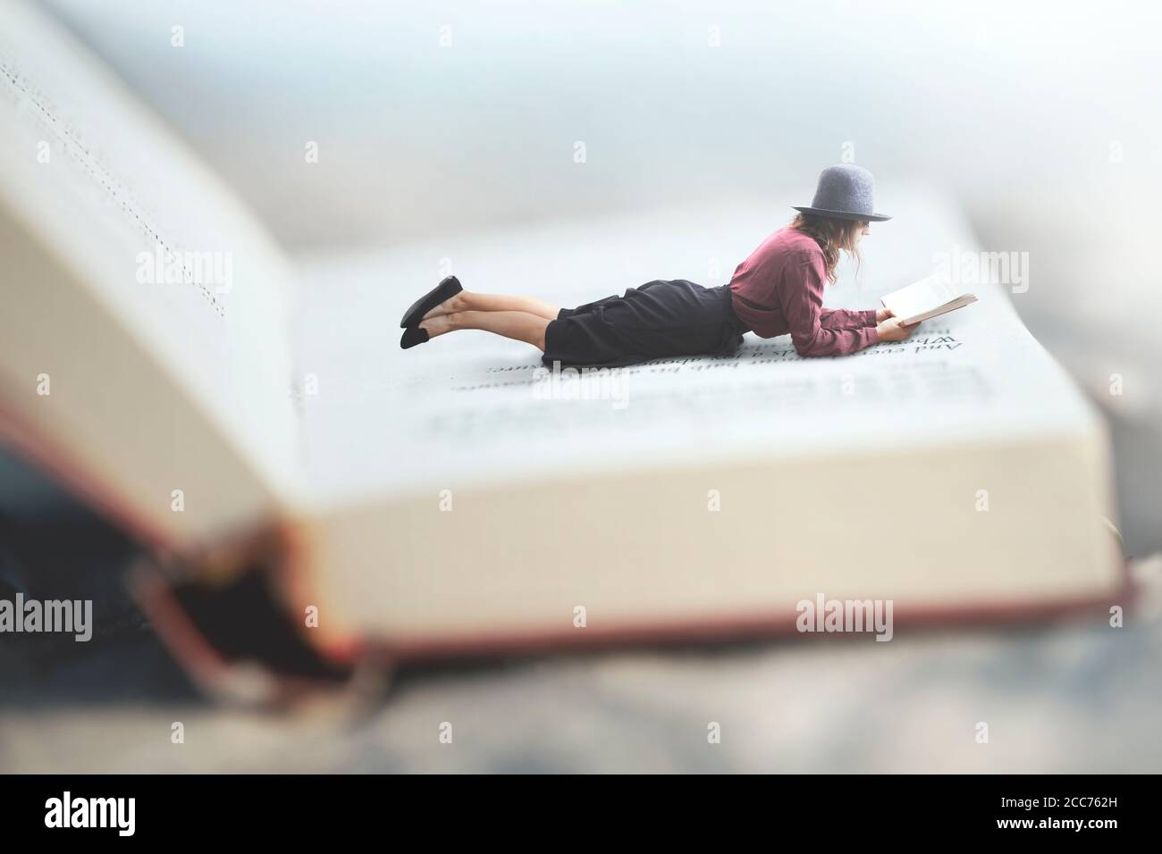 surreal situation of a woman reading her book lying on a giant book Stock Photo