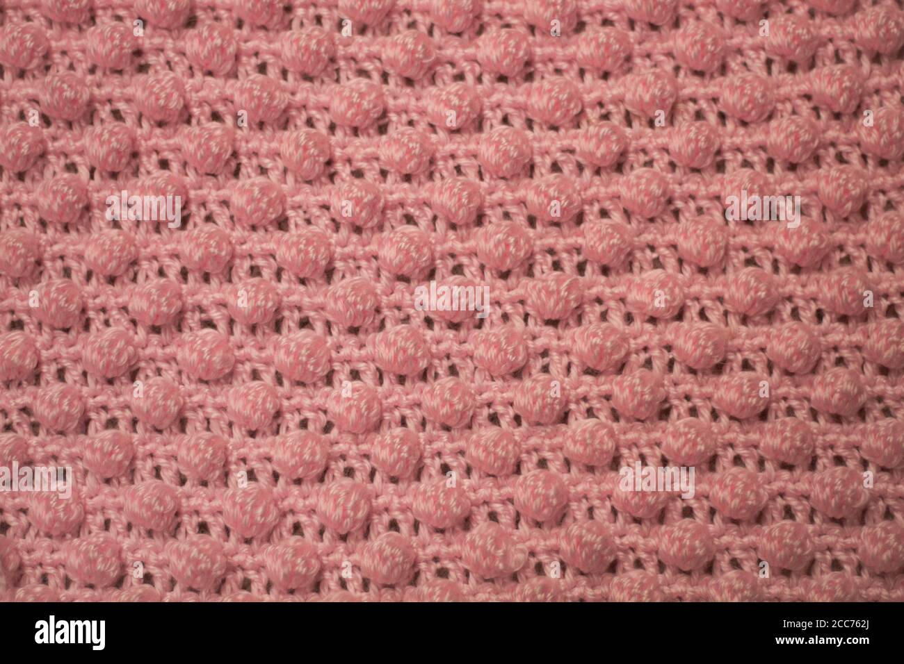 Textured pink background consisting of pink yarn crocheted baby blanket in the bobble stitch also know as the pineapple stitch Stock Photo