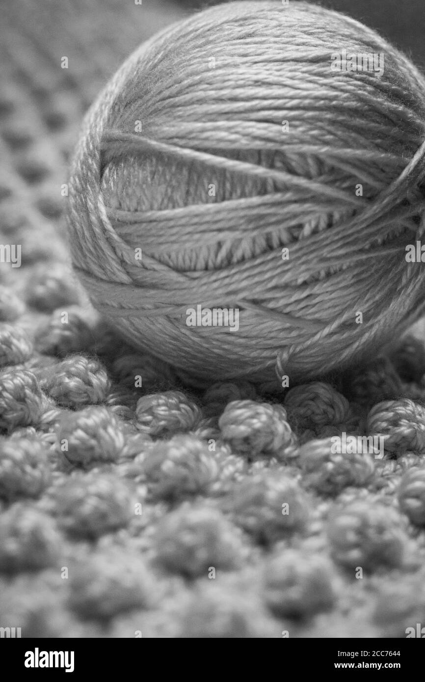 Black and white photograph of a ball of yarn with textured background consisting of crocheted baby blanket in the bobble stitch also known as the pine Stock Photo