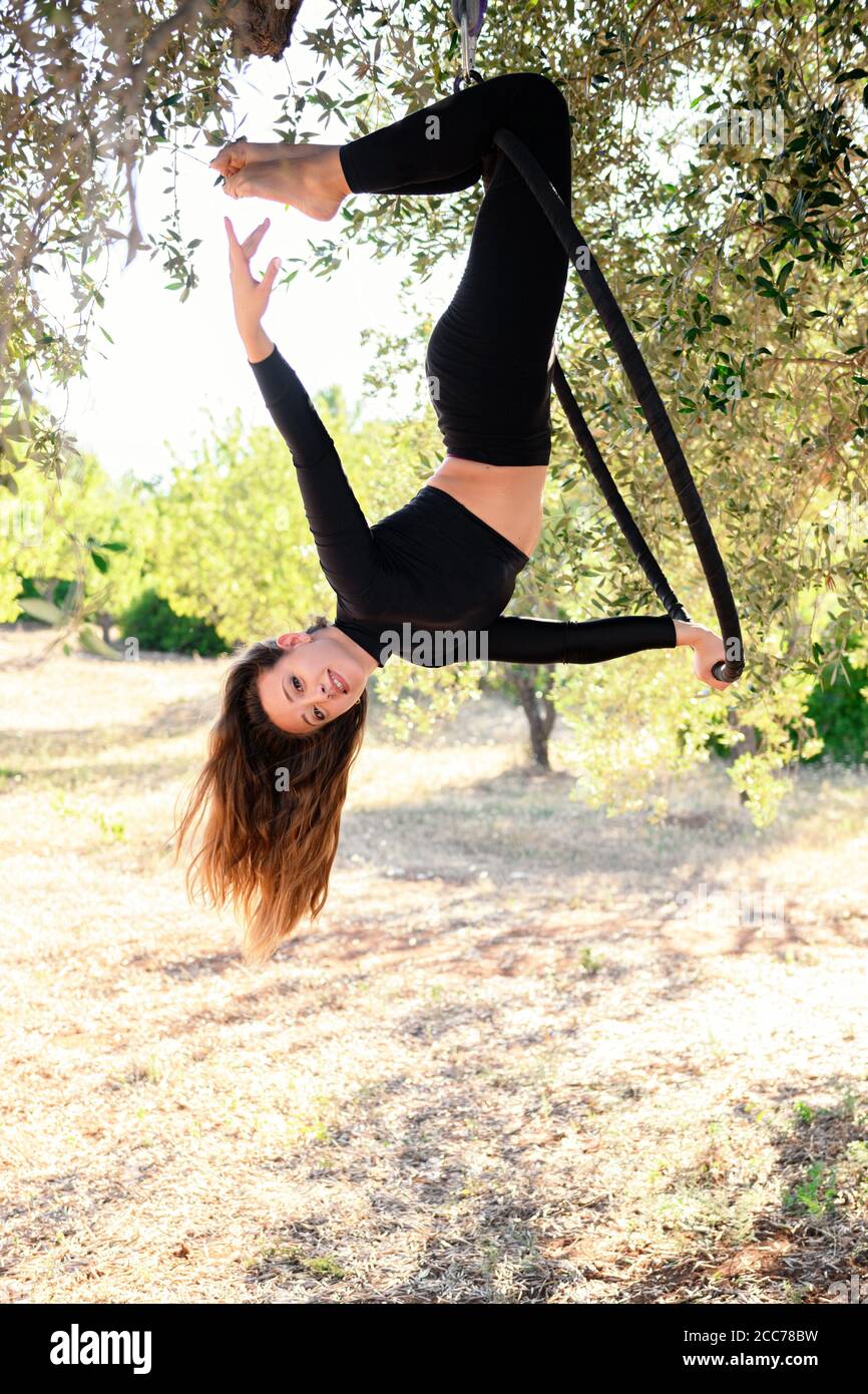 Acrobat making a pose on aerial hoop among olive trees in summer. Stock Photo