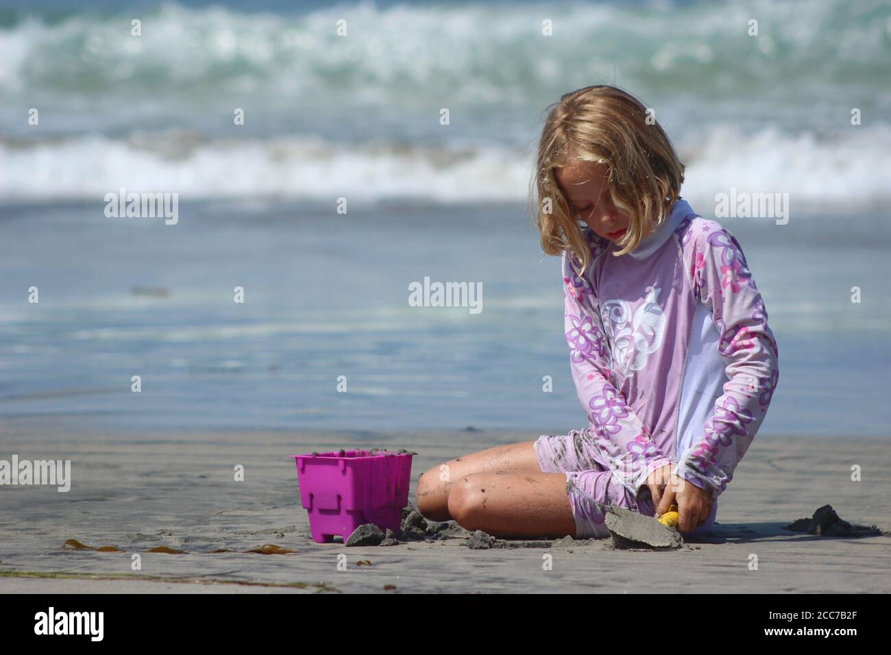 A young blond girl plays with sand toys at the beach Stock Photo