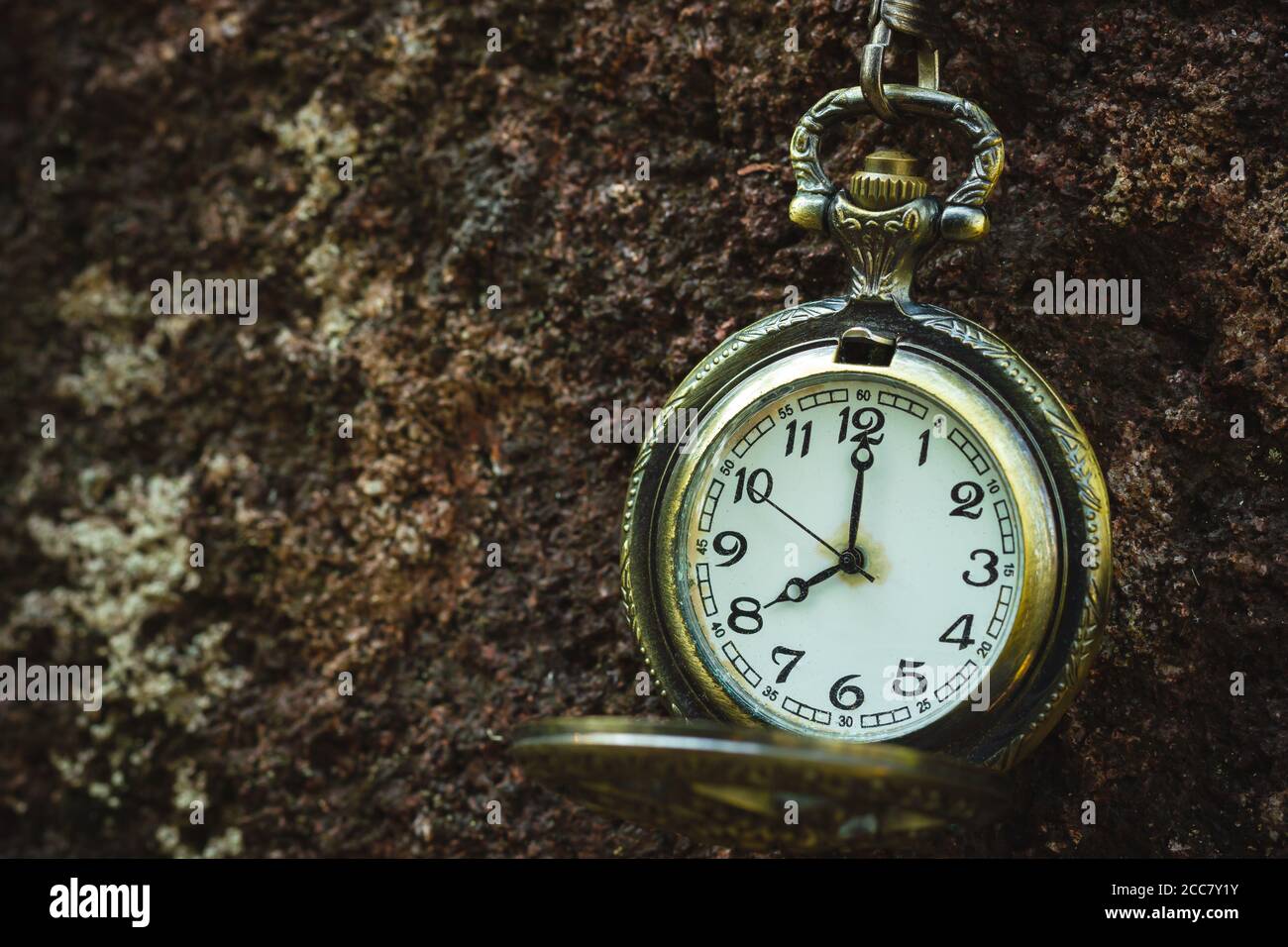 Vintage old pocket watch hanged on the rock background. At 8 o'clock. Closeup and copy space. Stock Photo