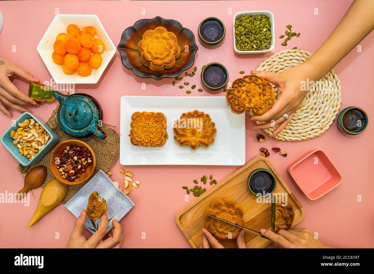 Hands of happy people eating tasty round moon cakes at mid autumn festival. Flat lay mid autumn festival food and drink on sweet pink background. Trav Stock Photo