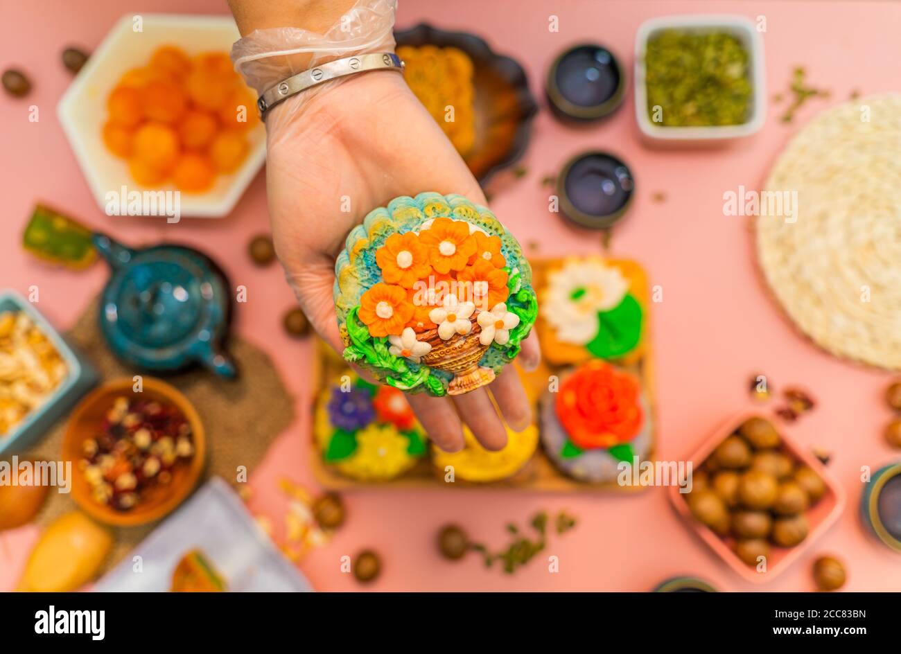 Hands of happy people eating tasty round moon cakes at mid autumn festival. Flat lay mid autumn festival food and drink on sweet pink background. Trav Stock Photo