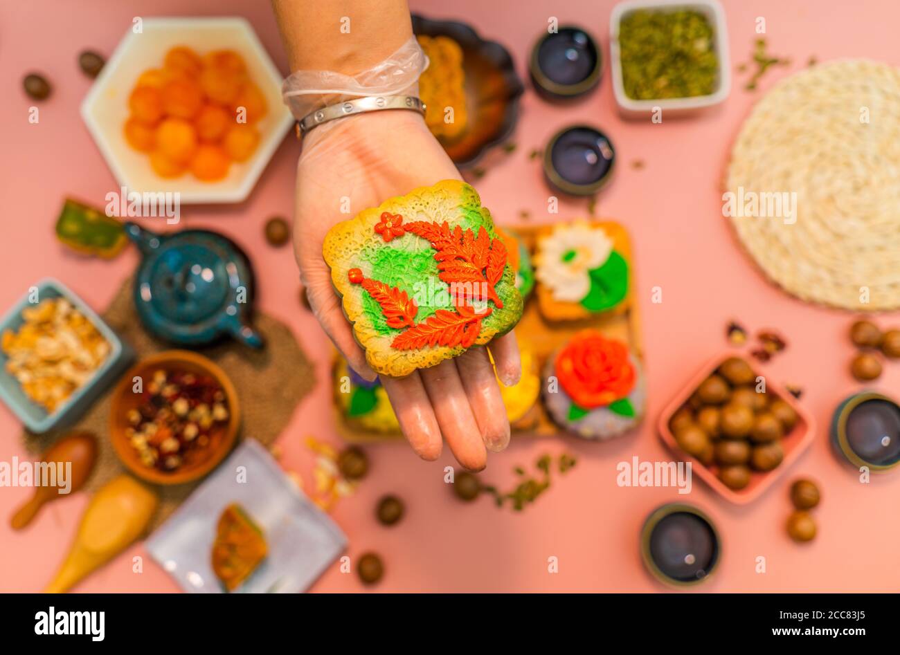 Hands of happy people eating tasty round moon cakes at mid autumn festival. Flat lay mid autumn festival food and drink on sweet pink background. Trav Stock Photo