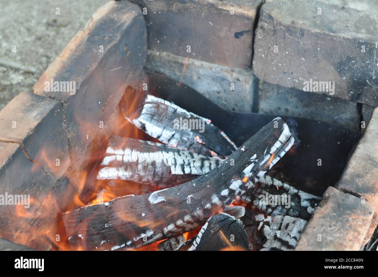 Burning firewood with flames over cracked logs covered with white ashes