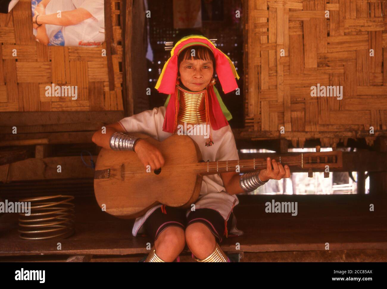 Thailand: Padaung (Long Neck Karen) woman plays a locally produced guitar in a village near Mae Hong Son, northern Thailand. The Padaung or Kayan Lahwi or Long Necked Karen are a subgroup of the Kayan, a mix of Lawi, Kayan and several other tribes. Kayan are a subgroup of the Red Karen (Karenni) people, a Tibeto-Burman ethnic minority of Burma (Myanmar). Stock Photo