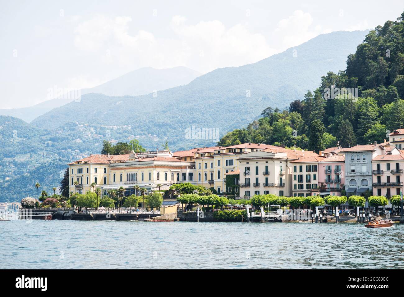 Bellagio City Skyline. Italy. Ferry Pier. Panoramic View from Lake Como with Alps. Morning. Cloudy Sky. Stock Photo