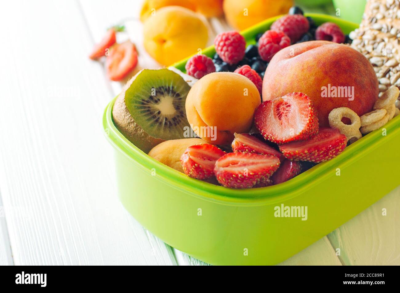 Lunch box with fruits, berries and crunches on white wooden background