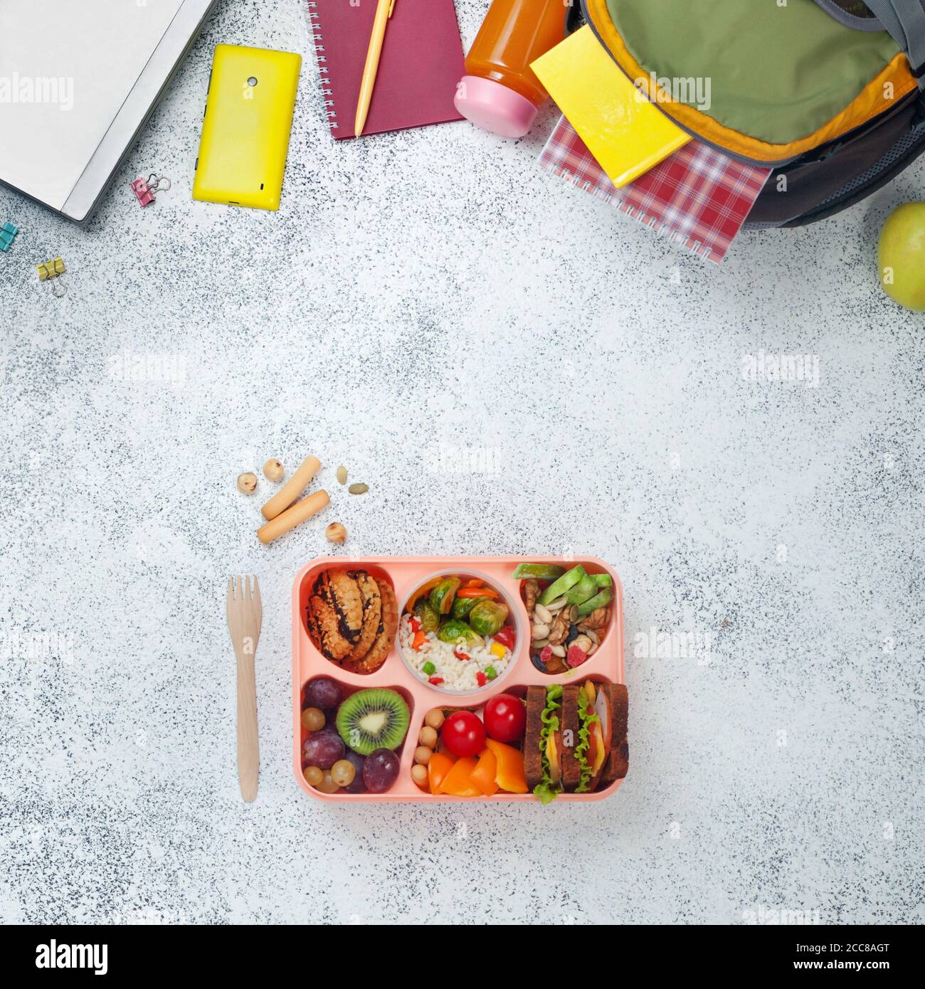 Open lunch box with healthy food near backpack and laptop on grey