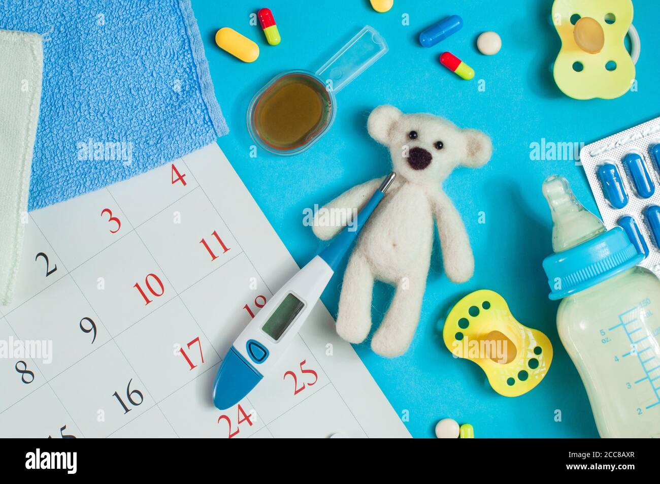 Pills and bear toy with electronic thermometer on blue backround near calendar page Stock Photo