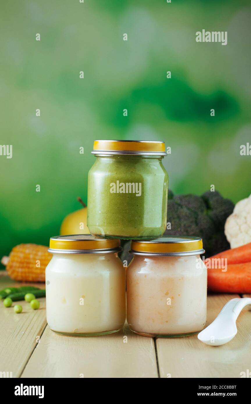 Three jars with puree with spoon near fresh fruits and vegetables Stock Photo