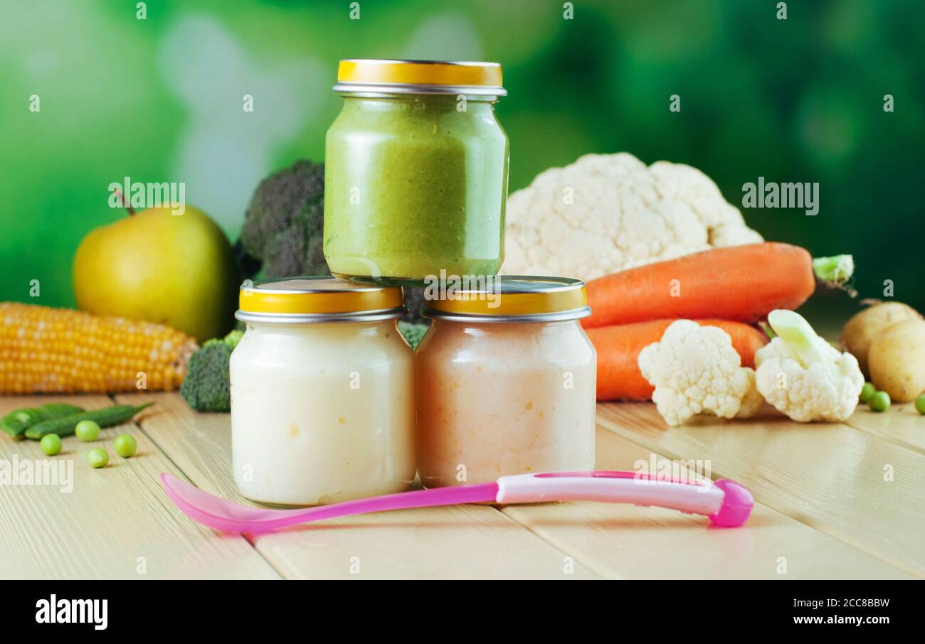 Three jars with vegetable puree on the light wooden background Stock Photo