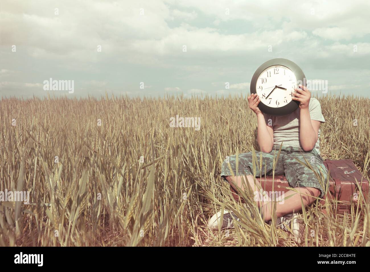 Boy on a trip hides his face with a clock in a desert landscape Stock Photo