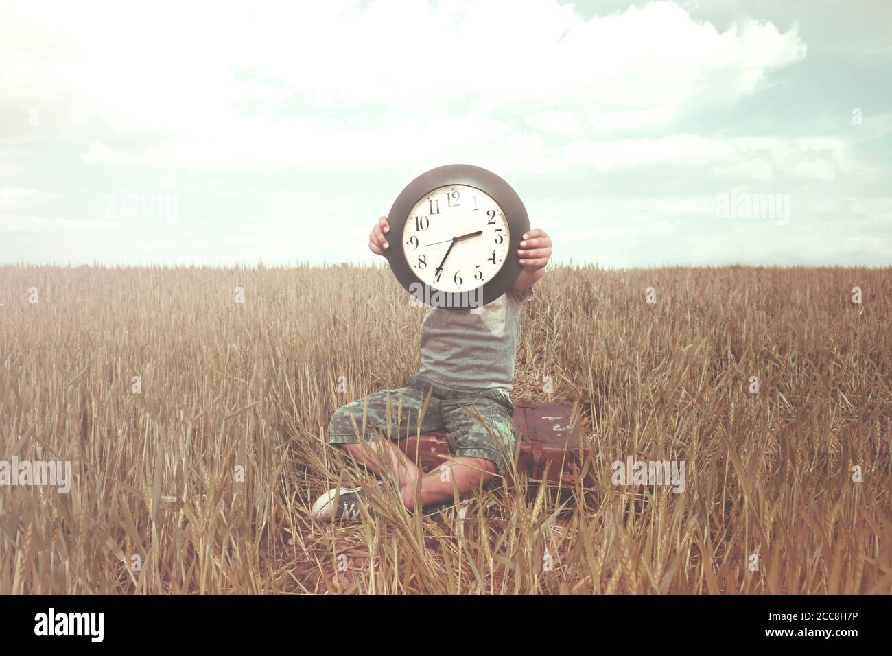 Boy on a trip hides his face with a clock in a desert landscape Stock Photo