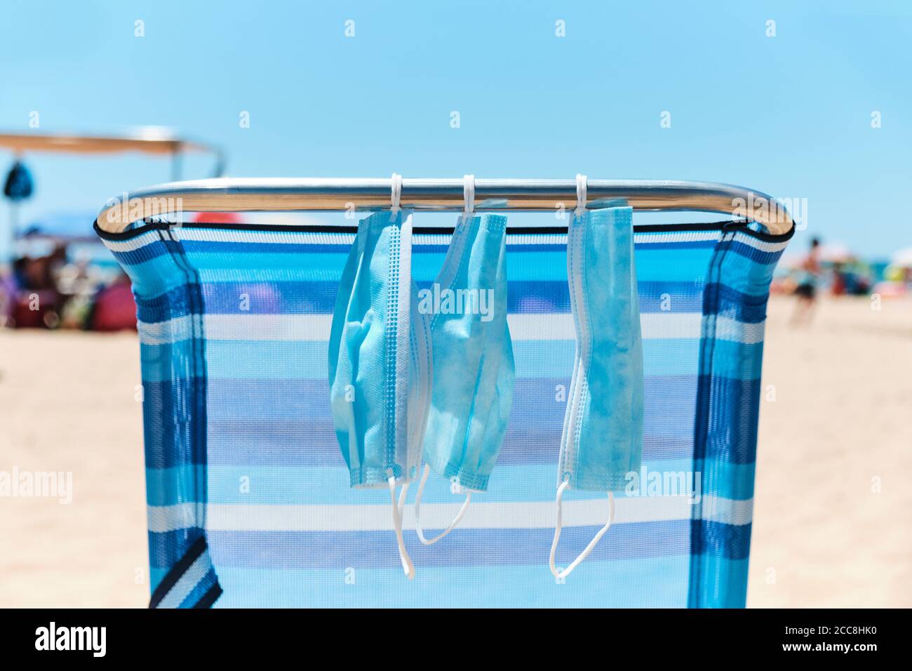 closeup of some blue face masks hanging from a blue deck chair on the beach Stock Photo
