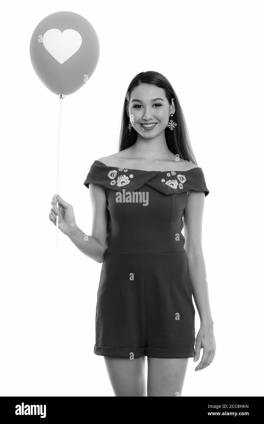 Studio shot of young happy beautiful Asian woman smiling and standing while holding balloon with heart sign Stock Photo