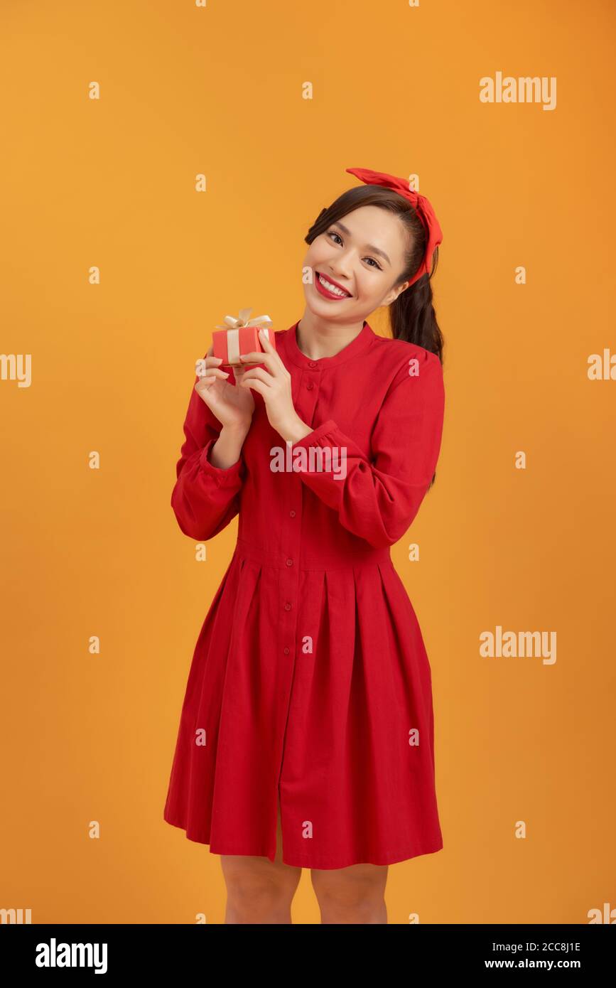 Cheerful young Asian woman holding gift box when standing over orange background. Stock Photo