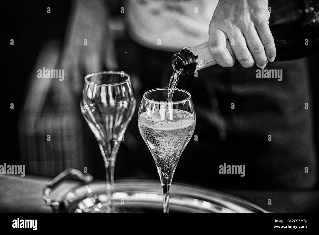 Woman bar tender hand seving sparkling white wine on two glasses for a toast Stock Photo