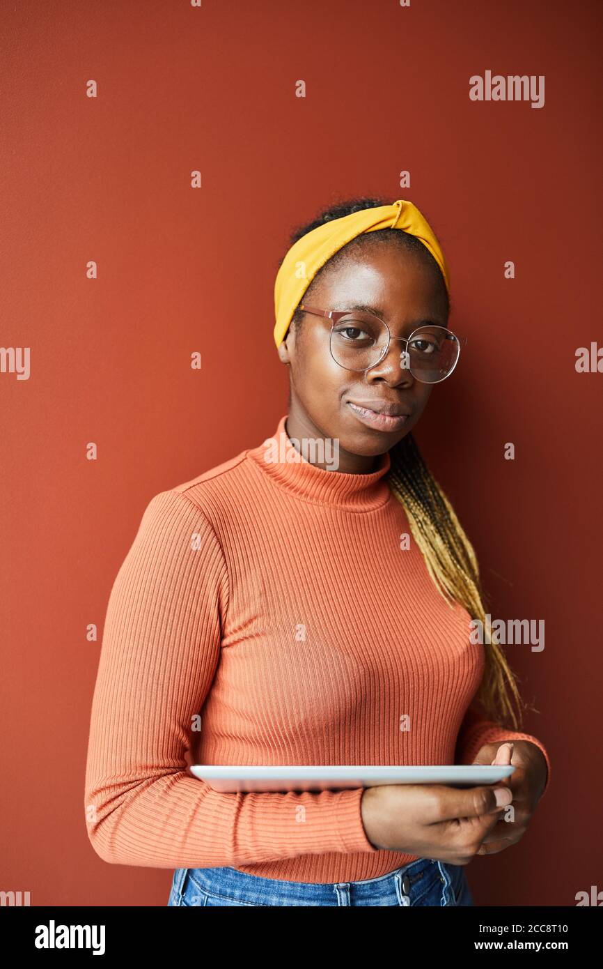 Portrait of African young woman with beautiful hairstyle holding digital tablet and looking at camera isolated on brown background Stock Photo