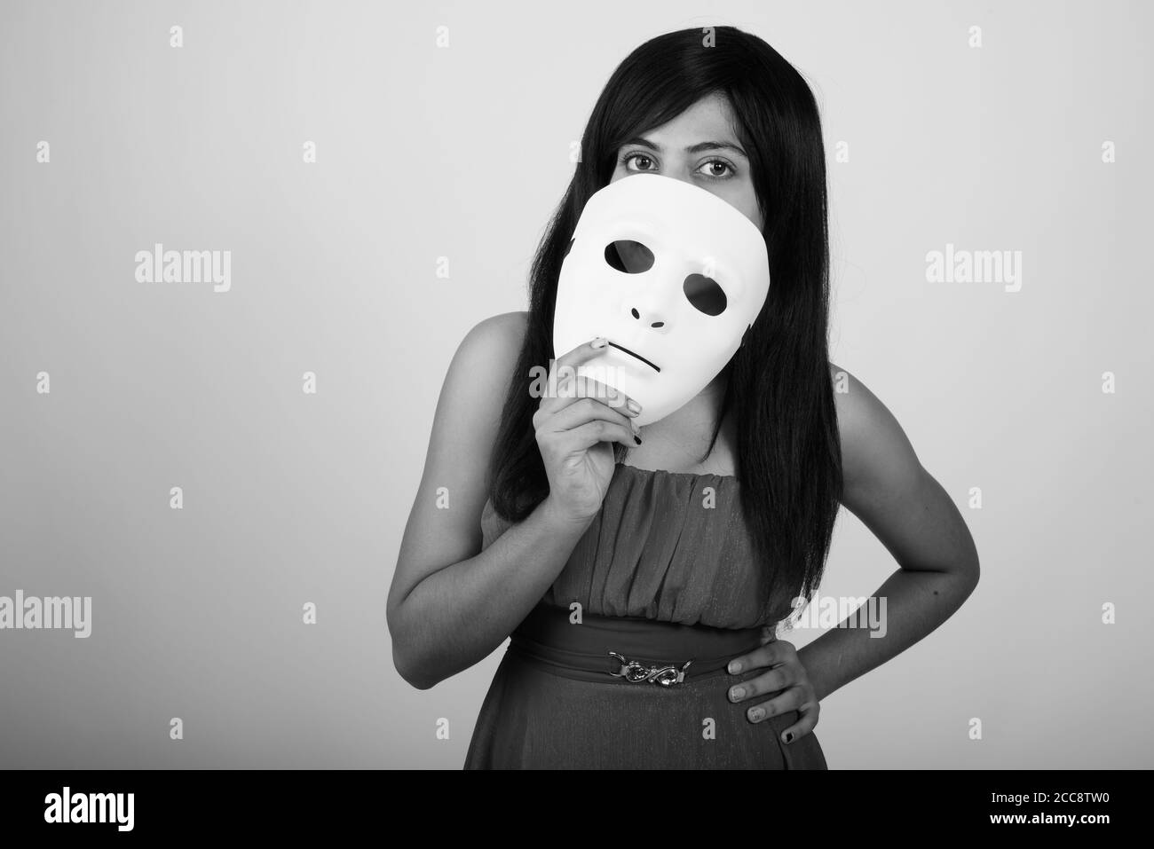 Studio shot of young Persian woman covering face with white mask against gray background Stock Photo