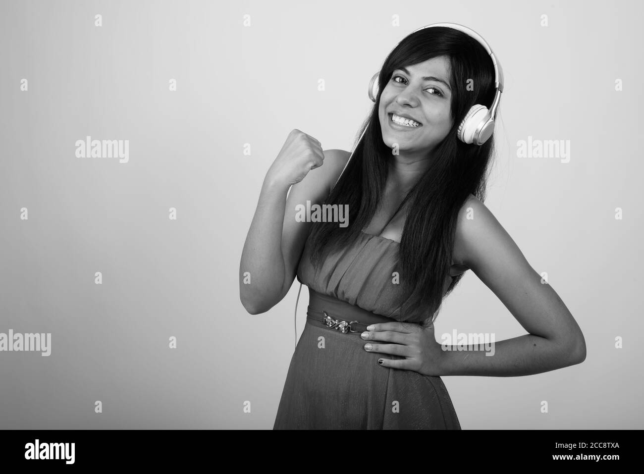Studio shot of young happy Persian woman smiling while looking motivated and listening to music against gray background Stock Photo