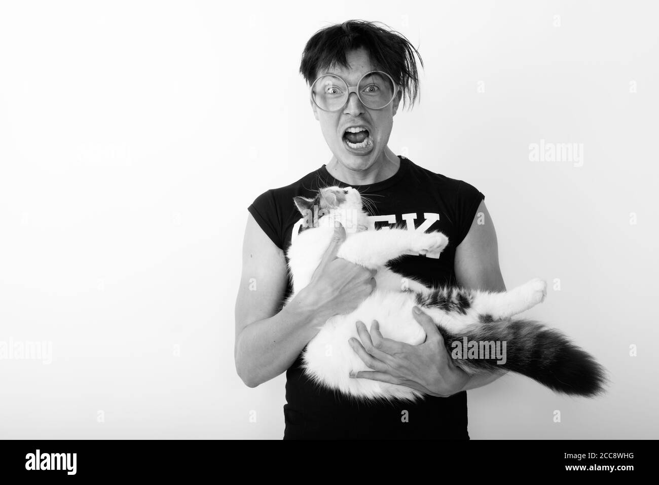Studio shot of young nerd man looking excited while holding cute cat and wearing eyeglasses Stock Photo