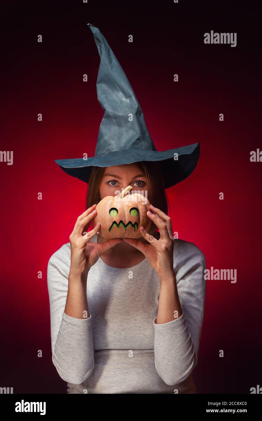 Halloween A Young Woman In A Black Witch Hat Is Holding A Pumpkin With A Zombie Face Vertical Stock Photo Alamy