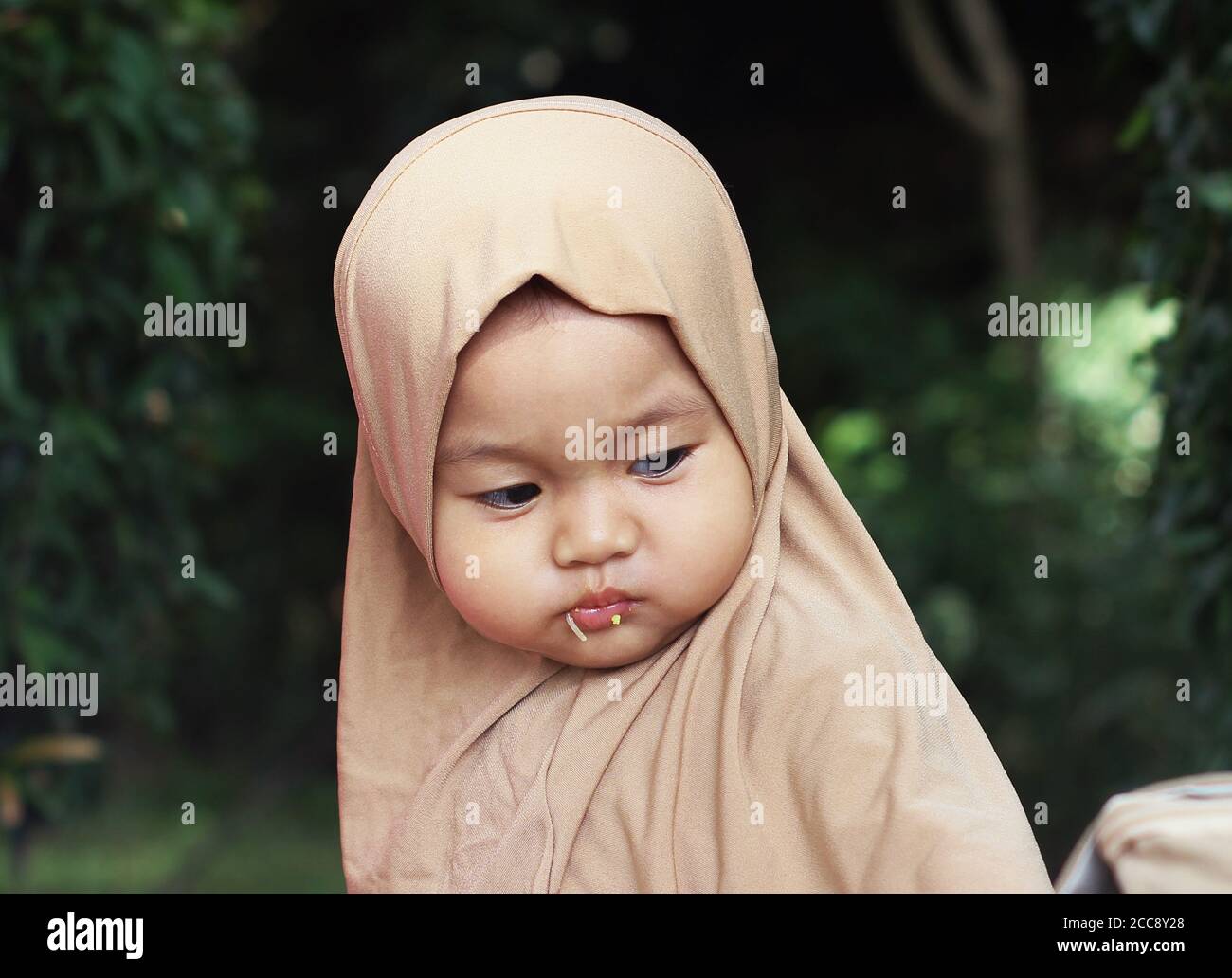 A cute beautiful muslim Indonesian baby chewing food Stock Photo